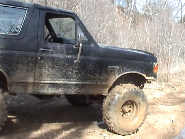Black Ford Bronco with large tires, covered in mud, seen from the side