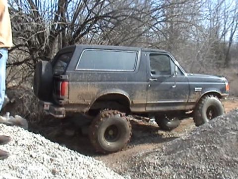 1991 Ford Bronco - A 1991 Ford Bronco navigates a rough, off-road terrain with muddy tires.