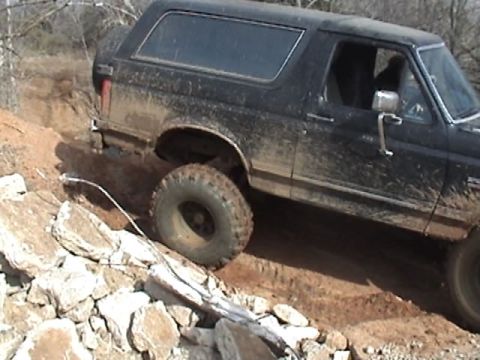 1991 Ford Bronco - A black Ford Bronco navigates a rocky, off-road path, kicking up dirt.