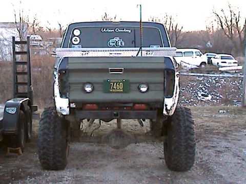 1977 Ford F-150 - Rear view of a lifted 1977 Ford F-150 with custom modifications and a trailer hitch. Other vehicles are parked in the background.