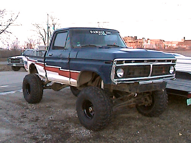 Dark blue lifted pickup truck with red and white stripe on the side. "DAMAGE INC" text on windshield