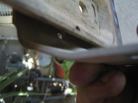 1990 Ford Bronco - hand holds a folded bare-metal panel edge in the foreground with a cluttered engine bay and greenery blurred behind it.