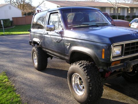 1986 Ford Bronco II - Dark blue SUV with lifted suspension and large tires parked on a residential street.
