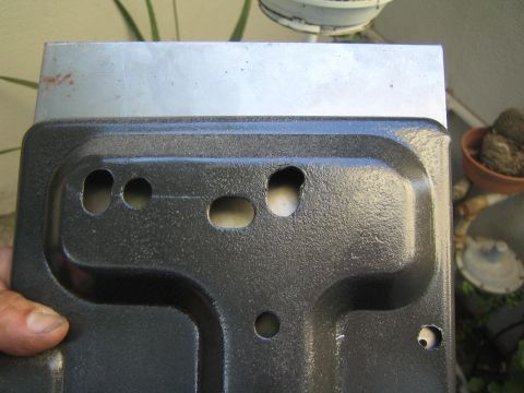 1990 Ford Bronco - hand holds a black wrinkle-coated stamped sheet-metal tray with several mounting holes, photographed by potted plants and a stucco wall.