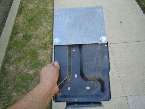 1990 Ford Bronco - hand holds a black wrinkle-finish stamped tray with a flat metal plate bolted to its top flange, over a sidewalk and lawn.