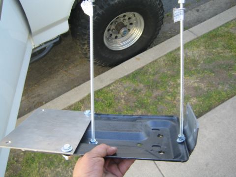 1990 Ford Bronco - black-coated metal tray hangs on two threaded rods below a flat plate held by a hand, with an off-road truck wheel in the background.