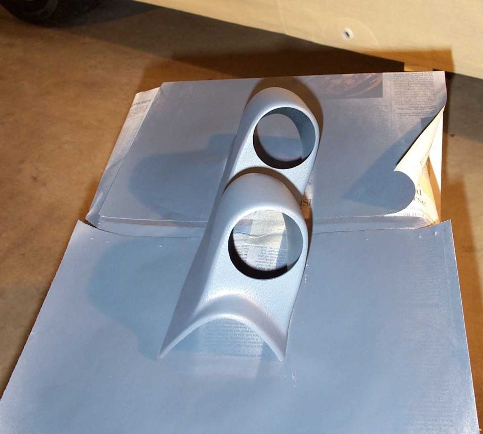 Gray-painted dual gauge pod trim piece drying on newspaper in a box