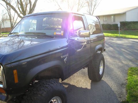 1986 Ford Bronco II - A dark blue Ford Bronco II with lifted suspension and large tires is parked on a street.