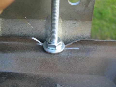 1990 Ford Bronco - zinc-plated hex bolt with a threaded rod and washer is fastened through a brown coated metal bracket, shot close-up outdoors.