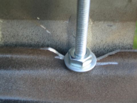 1990 Ford Bronco - Close-up of a zinc hex nut, washer, and threaded rod clamping down on a brown wrinkle-coated metal bracket with reference scribe lines.