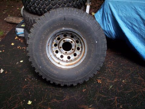 1991 Ford Bronco - A BFGoodrich Mud-Terrain T/A tire mounted on a multi-hole rim is shown, with other tires stacked in the background.
