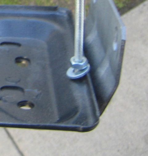 1990 Ford Bronco - Tight crop of a black-coated stamped metal tray corner with a zinc bolt and washer on a threaded rod, over a concrete background.