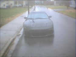 1993 Ford Probe - A dark sedan with pop-up headlights is parked on the side of a wet street.