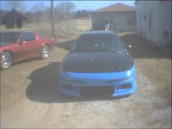 1993 Ford Probe - A blue and black car with a modified front bumper sits in a dirt lot next to a red car.