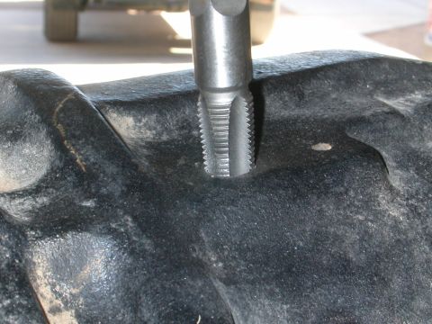 1984 Ford Bronco - A tap tool is used to thread a black metal component, with a blurry vehicle in the background.