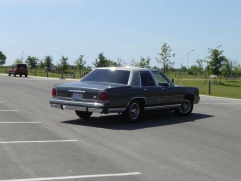 1988 Ford LTD Crown Victoria - A dark gray 1988 Ford Crown Victoria LTD sedan is parked in a lot with another vehicle in the background.