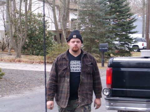 2006 Ford F1 - A man wearing a plaid shirt and beanie stands in front of a black pickup truck, with another white vehicle visible in the background.