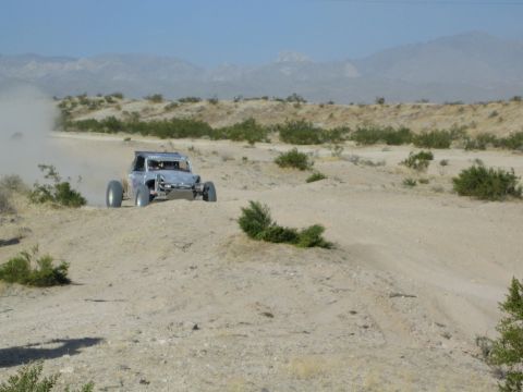 Silver tube-frame off-road buggy racing along a sandy desert trail