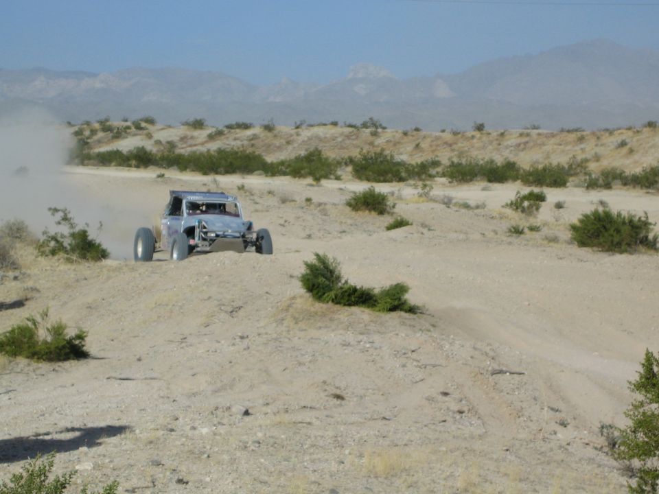 Silver tube-frame off-road buggy racing along a sandy desert trail