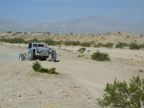 Silver tube-frame off-road buggy catching air over a desert berm