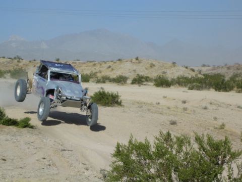 Purple and white off-road buggy jumping over a desert rise