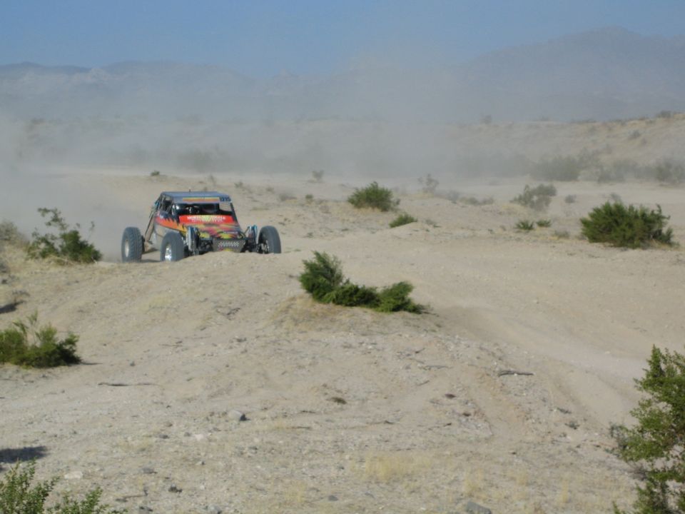 Orange and black off-road buggy racing across a dusty desert trail