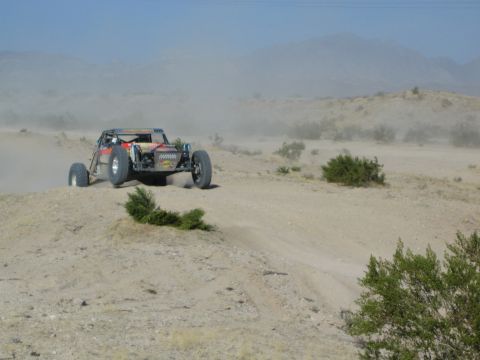 Orange and black off-road buggy catching air over a desert berm