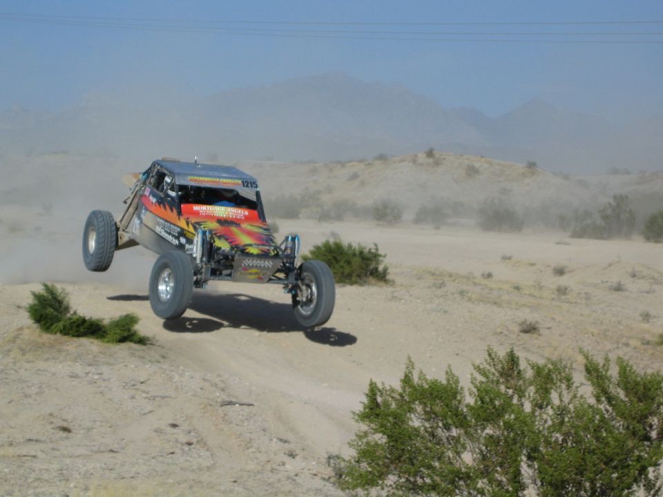 Brightly painted off-road buggy number 1215 jumping over a desert rise