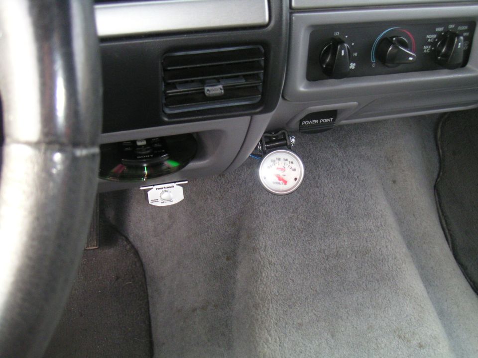 Aftermarket white-face voltmeter gauge mounted under gray dash beside HVAC controls