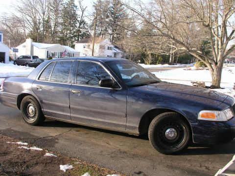 1999 Ford Crown Victoria - A dark blue sedan sits on a driveway with snow on the ground and trees in the background.