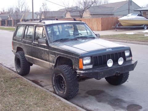 1993 Jeep Cherokee - A lifted 1993 Jeep Cherokee with large off-road tires is parked on a residential street.