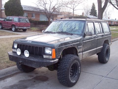 1993 Jeep Cherokee - A muddy 1993 Jeep Cherokee is parked on the street, with another SUV in the background.