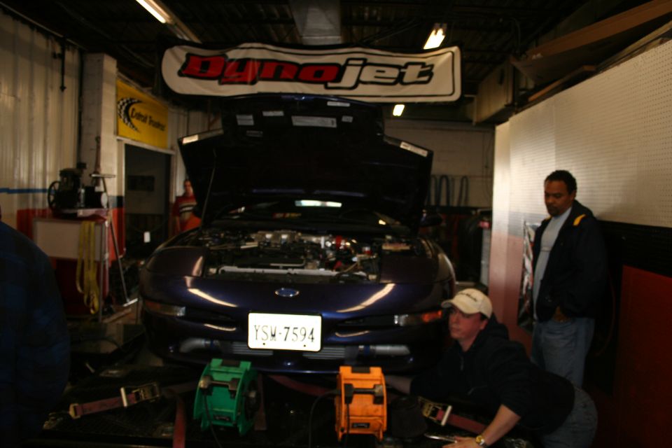 Dark blue coupe on dynamometer, hood open. License plate YSM-7594