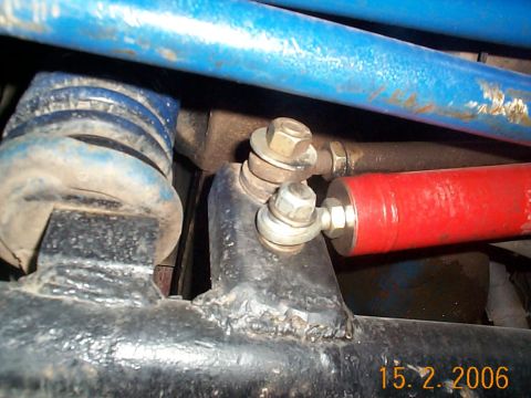 1977 Ford Bronco - A close-up of front steering and suspension components: stacked tie-rod ends bolted to a steering arm, a red steering stabilizer, and blue-…