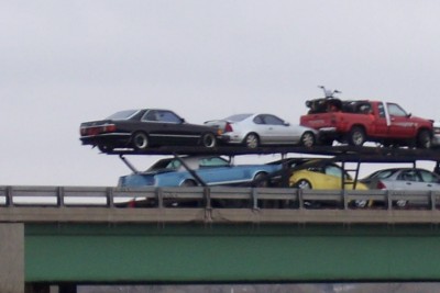 1972 Ford Ranchero - A car carrier truck transports several vehicles, including a black coupe, a white coupe, a blue convertible, a yellow car, and a red pickup…