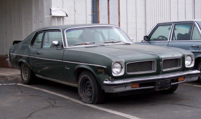 1972 Ford Ranchero - Green 1973 Pontiac Ventura has a flat front tire and is parked next to a dark blue sedan.