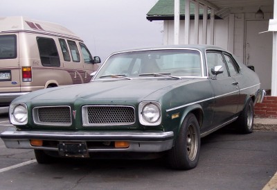 1972 Ford Ranchero - A green sedan with a split grille is parked in a lot next to a van.