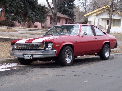 1972 Ford Ranchero - A red coupe with white racing stripes is parked on the side of a street.