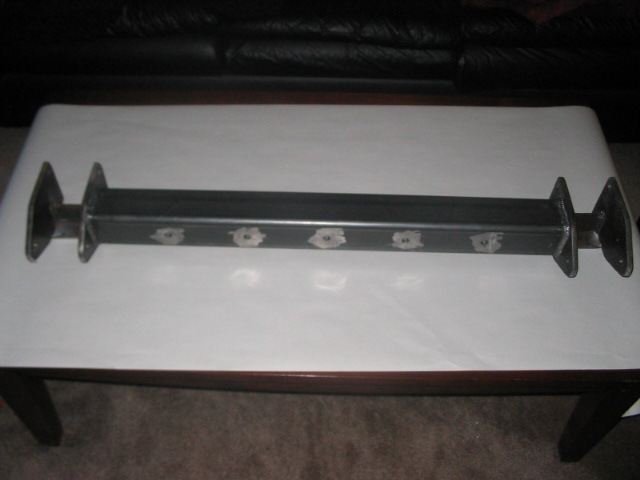 Custom metal axle with flange mounts on each end and six bolt holes along the body