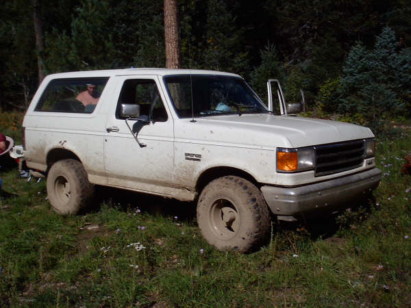1991 Ford Bronco parked on grassy, wooded terrain with front passenger door open