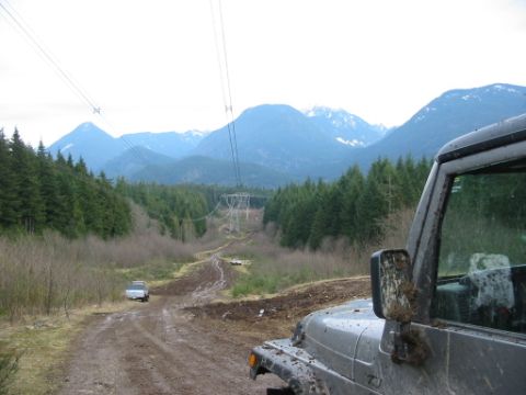1985 Ford F-150 - Off-roading scene with two vehicles on a muddy mountain trail under power lines.