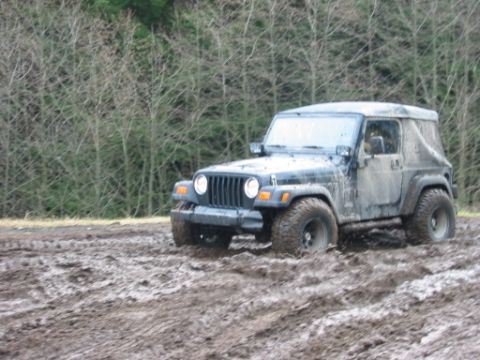 1985 Ford F-150 - A muddy Jeep Wrangler navigates through a challenging off-road terrain.