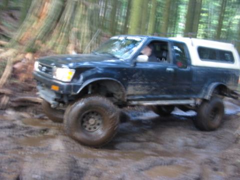 1985 Ford F-150 - Pickup truck navigates a muddy off-road trail in a wooded area.