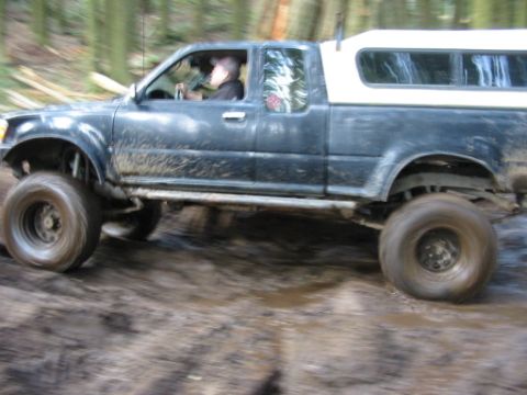 1985 Ford F-150 - A lifted pickup truck navigates a muddy off-road course with trees in the background.