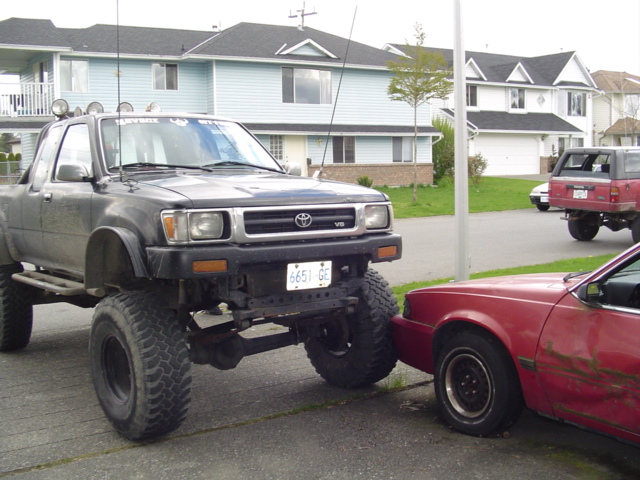 Black lifted Toyota pickup truck with large tires, front view, parked next to a red car