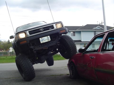 1985 Ford F-150 - A heavily modified Toyota pickup truck is resting on top of a red sedan.