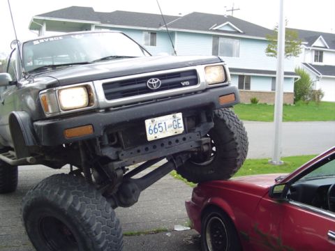 1985 Ford F-150 - A lifted Toyota truck is parked on top of a red car.