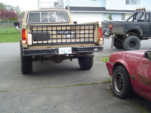 1985 Ford F-150 - Tan Ford F-series truck parked next to a black lifted truck and a red car.