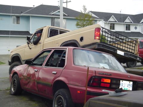 1985 Ford F-150 - A tan pickup truck is parked on top of a red sedan with significant damage to its side.