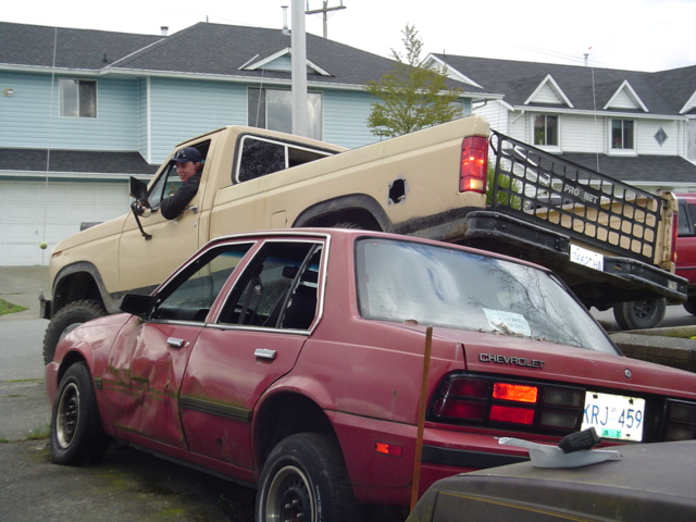 tan pickup truck with a man driving, parked over a damaged red sedan